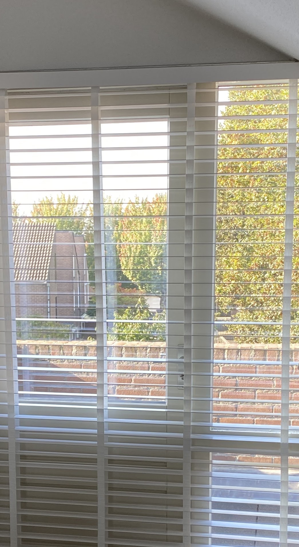 Witte houten jaloezieën voor een hoge raampartij op zolder