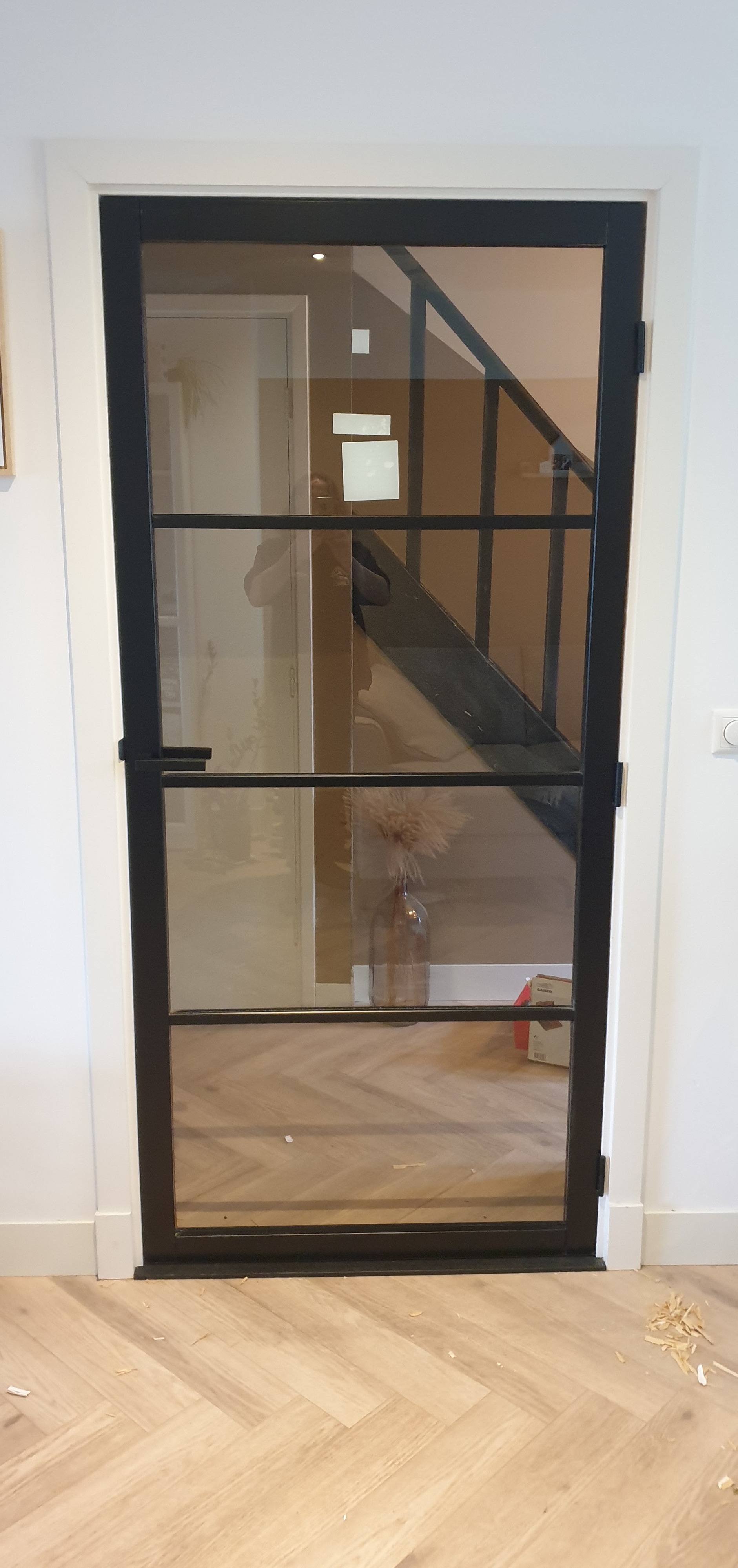 Zwarte stalen-look binnendeur met glas boven een visgraatvloer