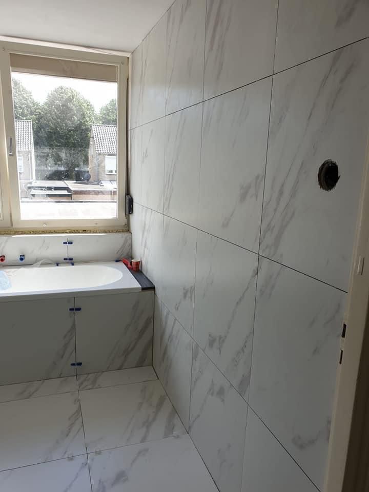 Badkamer met grote marmerlook tegels en een ingebouwd bad
