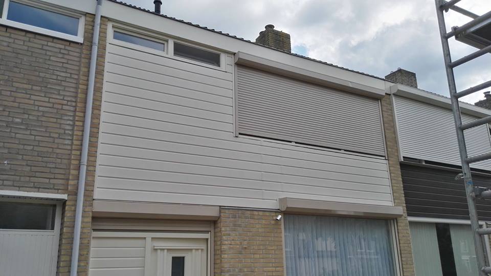 Gevel bekleed met witte kunststof schroten boven een voordeur